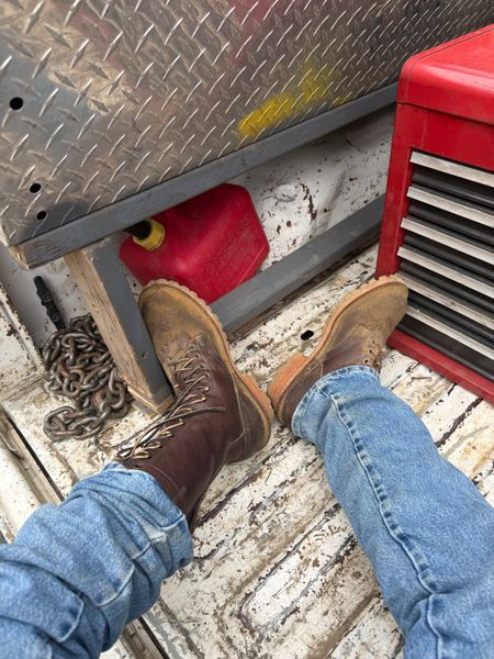 Person wearing jeans and brown work boots standing on a boat deck with red equipment and metal diamond plate flooring