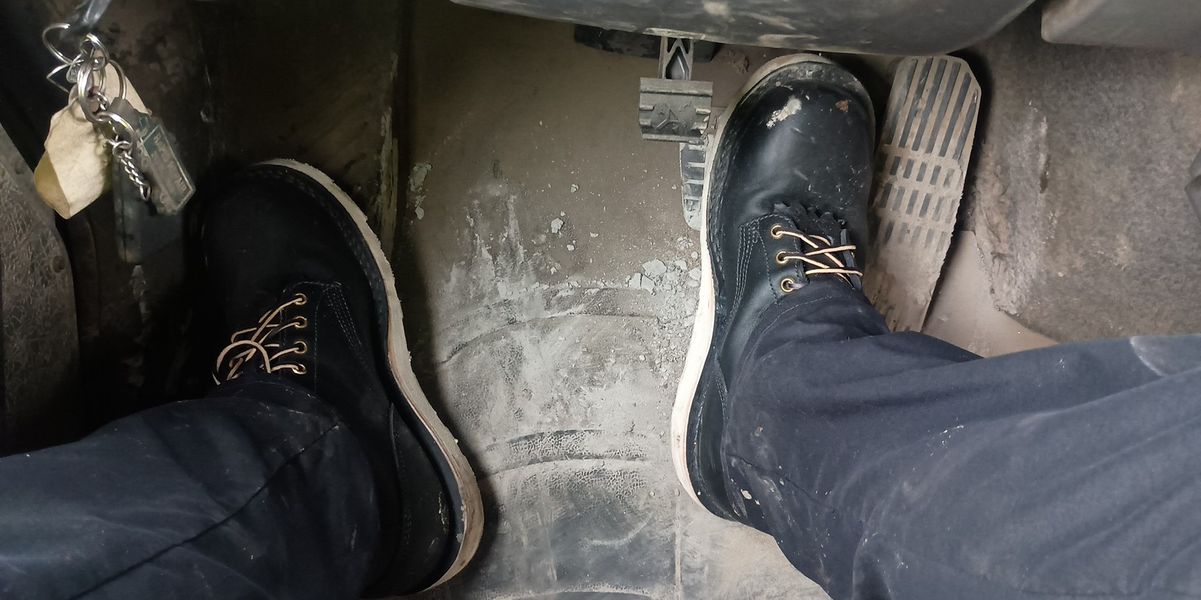 Person wearing dark boots sitting in driver's seat of vehicle with foot on brake pedal