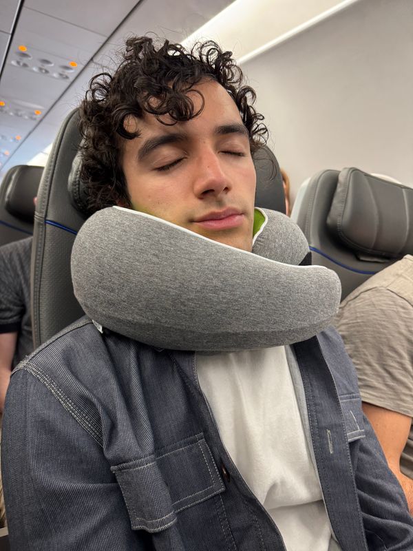 Customer sleeping on an airplane with a gray travel pillow