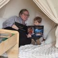 A woman and child reading a Christmas book together inside a cozy blanket fort or tent