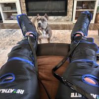 Customer-uploaded image. Click to see more details. The image represents: Person wearing leg compression therapy devices while relaxing at home with their pit bull dog nearby and a fireplace in the background