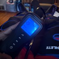 Customer-uploaded image. Click to see more details. The image represents: A handheld electronic device with a blue LCD screen displaying settings, being held in someone's hands in a living room setting