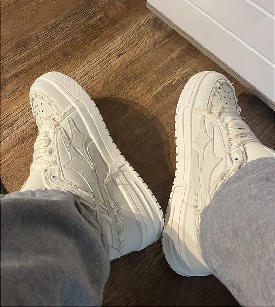 Person wearing white sneakers and gray sweatpants standing on wooden floor