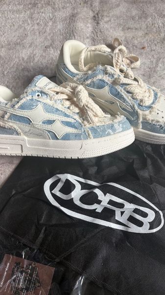 A pair of light blue and cream colored sneakers with rope laces sitting on top of a black bag with white text