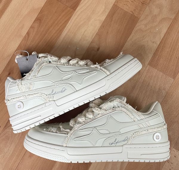 A pair of white sneakers with frayed, distressed details and rope-like laces sitting on a wooden parquet floor