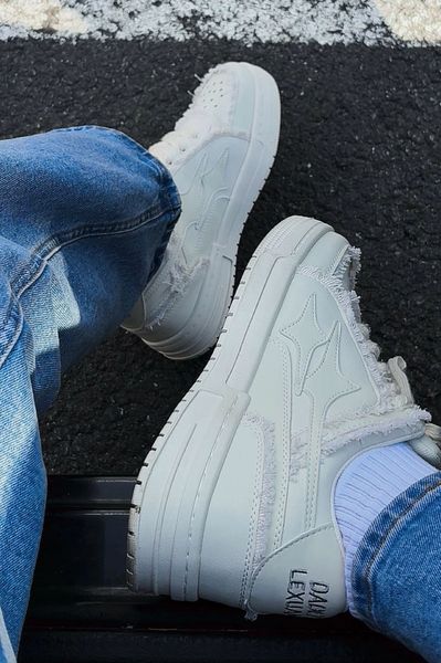 Person wearing white sneakers and blue jeans sitting on dark pavement