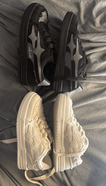 Two pairs of sneakers on fabric - one black pair and one cream/beige pair, both featuring similar star-like designs on the sides