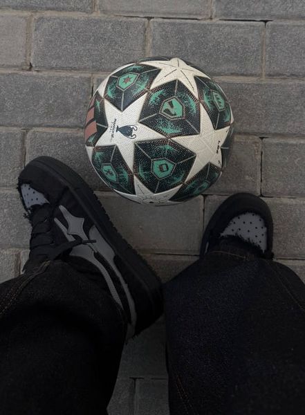 Soccer ball with green and white star pattern positioned between black athletic shoes on concrete ground