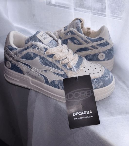 A pair of blue and white denim-patterned sneakers with white laces and soles, displayed with a black Decarba brand tag attached