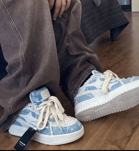 Person wearing brown sweatpants and blue and white patterned sneakers sitting on wooden floor