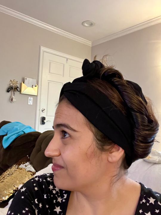 Woman wearing black headband with hair in messy bun sitting in living room
