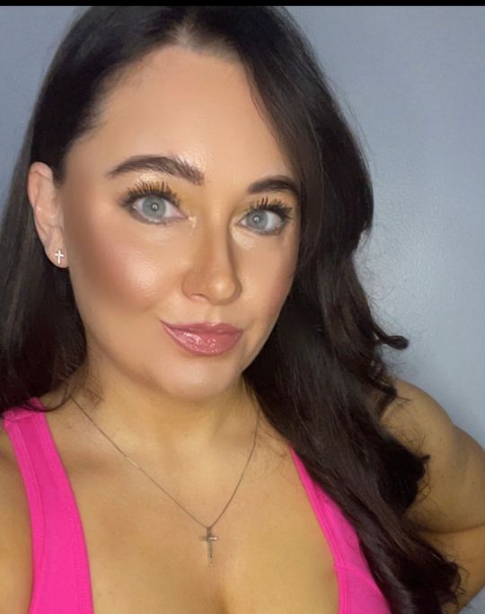 Woman with long dark hair wearing pink top and makeup taking a selfie