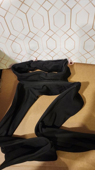 Black clothing items laid out on a wooden surface against a white wall with geometric hexagonal pattern