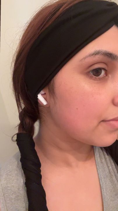 Person wearing white wireless earbuds with dark hair in a braid and black headband