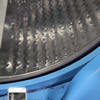 Customer-uploaded image. Click to see more details. The image represents: Interior view of a washing machine drum showing the perforated metal surface and blue exterior casing