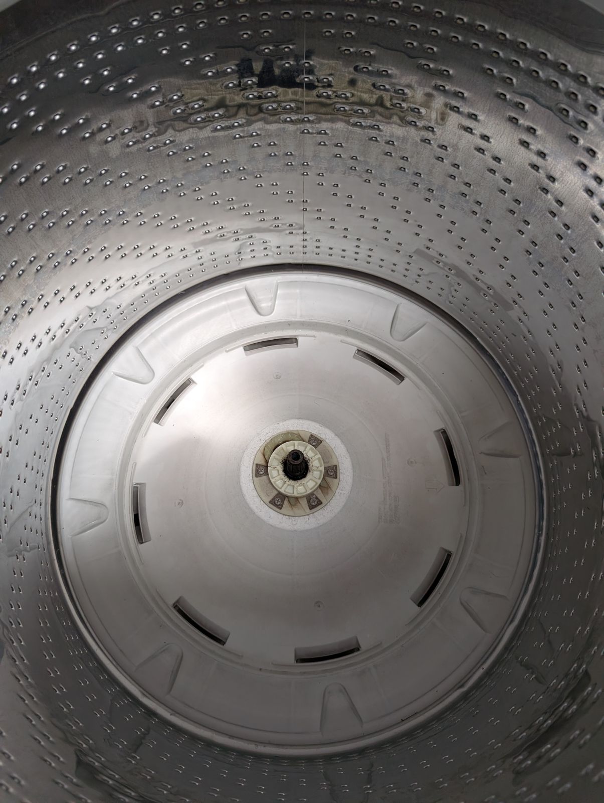 Interior view of a washing machine drum showing the perforated stainless steel walls and white plastic agitator at the bottom
