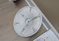 Customer-uploaded image. Click to see more details. The image represents: White circular washing machine drum or basket with perforated holes sitting on wooden floor next to instruction manual