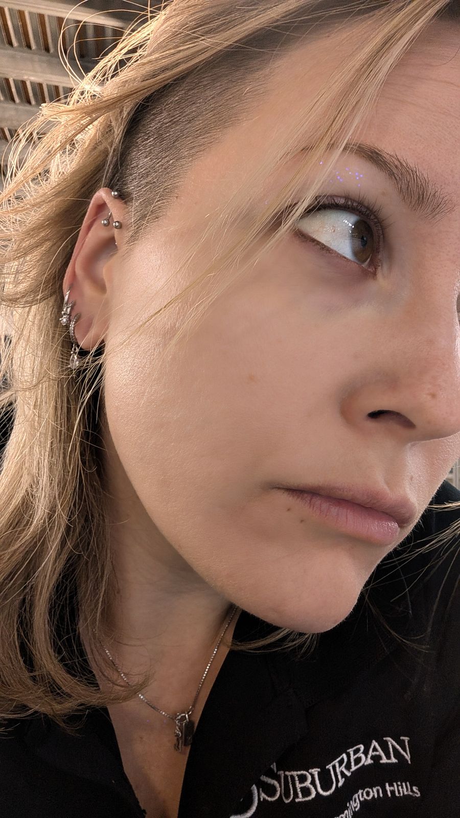 Close-up portrait of a young woman with blonde hair wearing multiple ear piercings and a black top with text