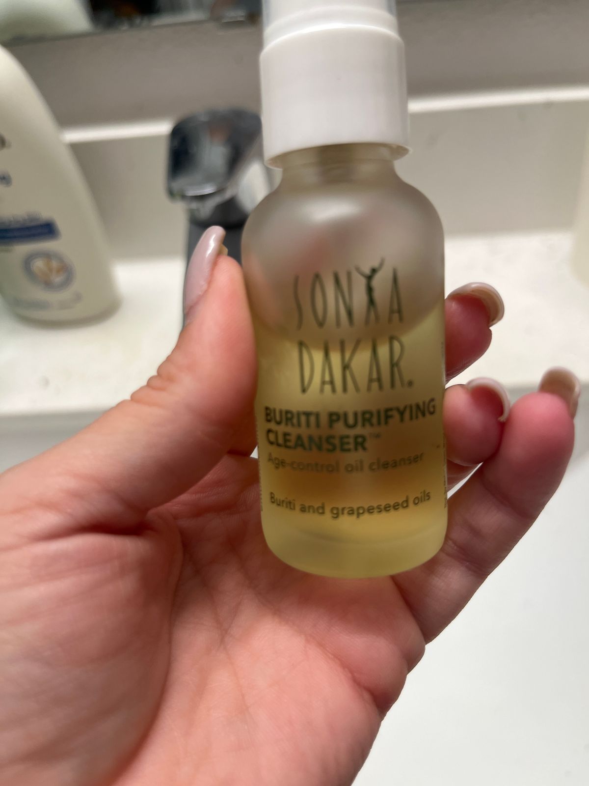A person holding a small bottle of Onyx Dakar Buriti Purifying Cleanser with a white cap, displaying the product label which mentions buriti and grapeseed oils as ingredients.