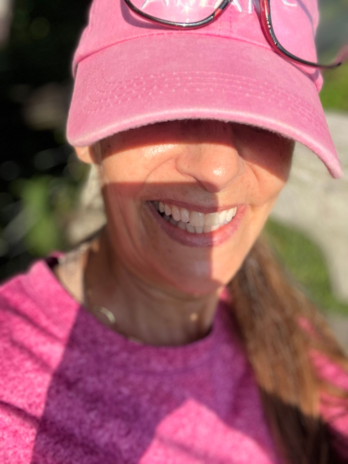 Person wearing pink cap and sunglasses smiling outdoors